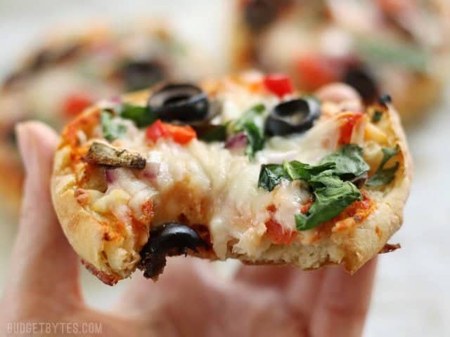 Make Ahead Frozen Mini Pizzas are an easy and inexpensive snack to keep stocked in your freezer. A healthier option to store-bought frozen pizza. BudgetBytes.com Close up of a baked Freezer Ready Mini Pizza with a bite taken out