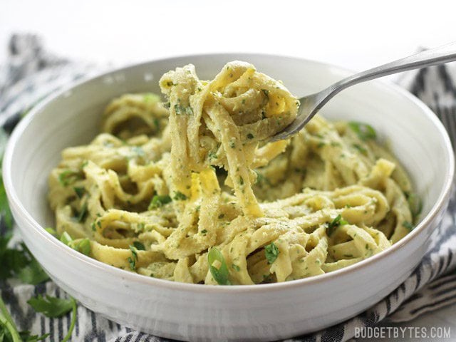 Fresh parsley scallion hummus makes a wonderfully creamy vegan pasta sauce for summer. Serve as a side dish or as the base for a bigger bowl meal. BudgetBytes.com A fork lifting some Parsley Scallion Hummus Pasta out of the bowl, viewed from the side