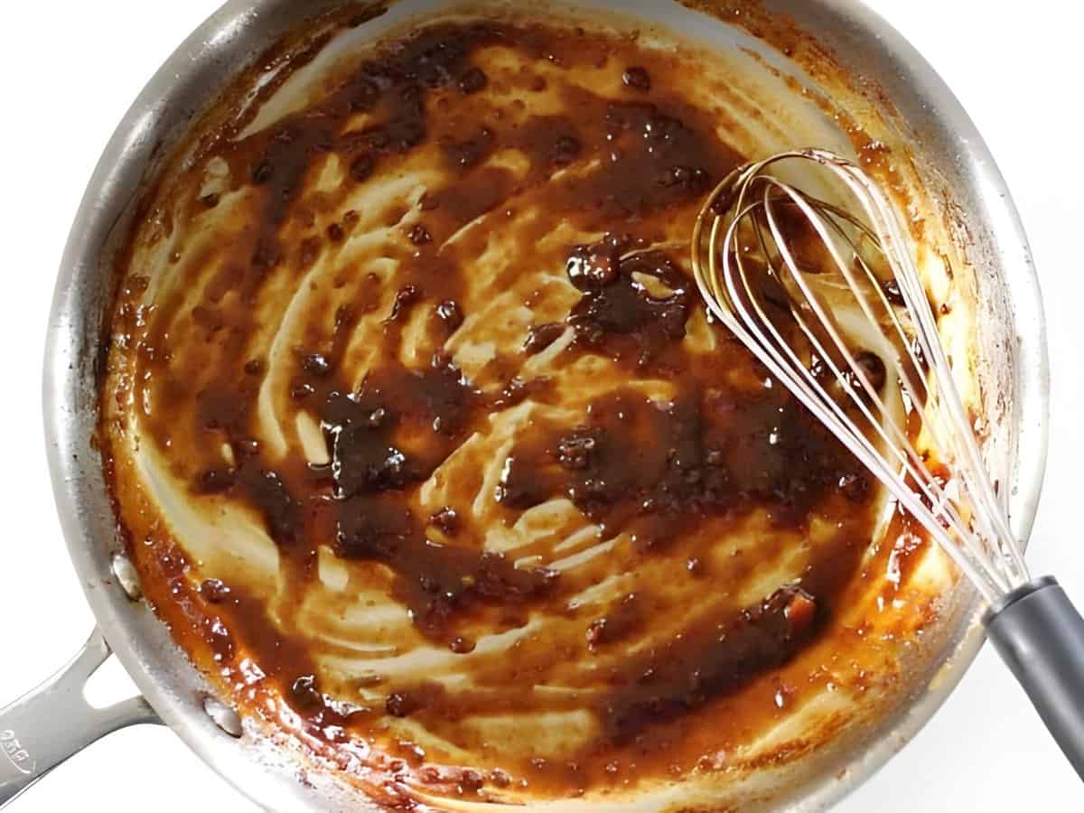 Sticky chicken marinade cooking in a skillet with a whisk.