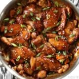 Sticky ginger soy glazed chicken in a skillet with sliced green onions.