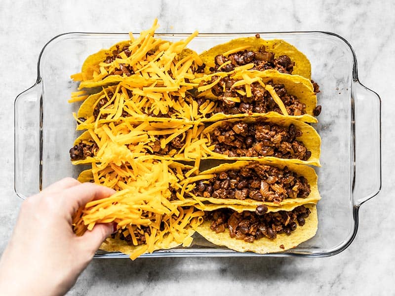 Taco shells being filled with beef and black bean mixture and topped with shredded cheese