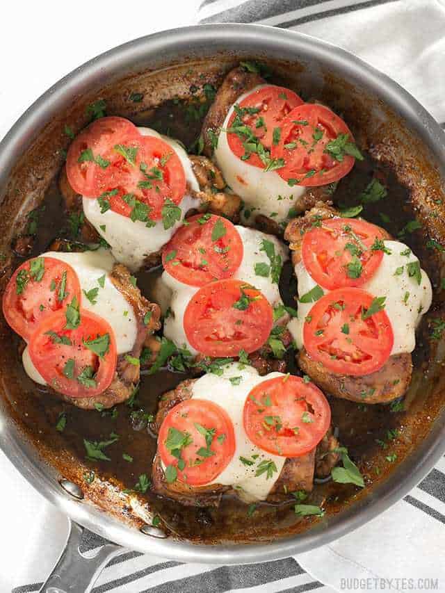 A simple marinade, creamy mozzarella, and fresh tomatoes turn simple chicken thighs into a fast and easy weeknight dinner in this Balsamic Chicken Skillet. BudgetBytes.com Overhead view of a skillet full of balsamic chicken thighs with melted mozzarella, fresh tomatoes, and chopped parsley on top.