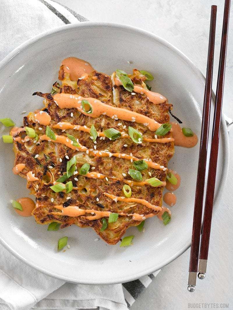 Savory Cabbage Pancakes are a fun and filling way to use up pantry leftovers. Fill them and top them with whatever your heart desires! BudgetBytes.com One savory cabbage pancake on a plate with sriracha mayo and chopsticks on the side.