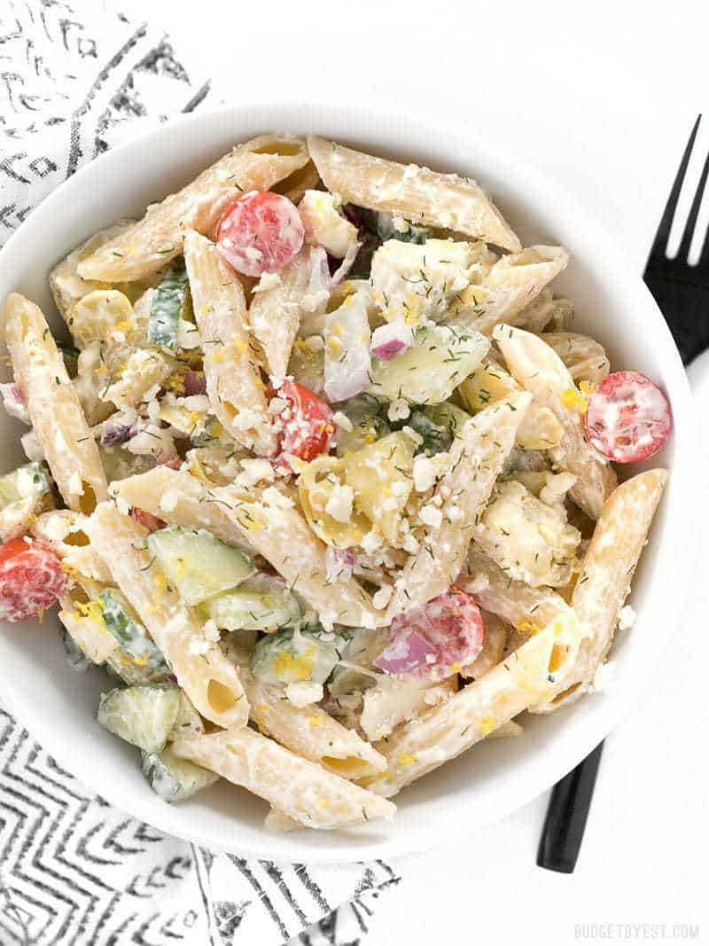 Creamy Lemon Dill Greek Pasta Salad is packed with bold flavors and fresh vegetables, making it a delicious light lunch or cold summer meal. BudgetBytes.com Overhead view of a bowl full of Creamy Lemon Dill Greek Pasta Salad