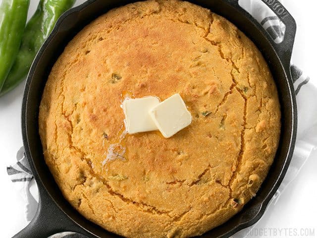 Top view of Hatch Chile Sweet Potato Cornbread in cast iron skillet, two cubes of butter on top