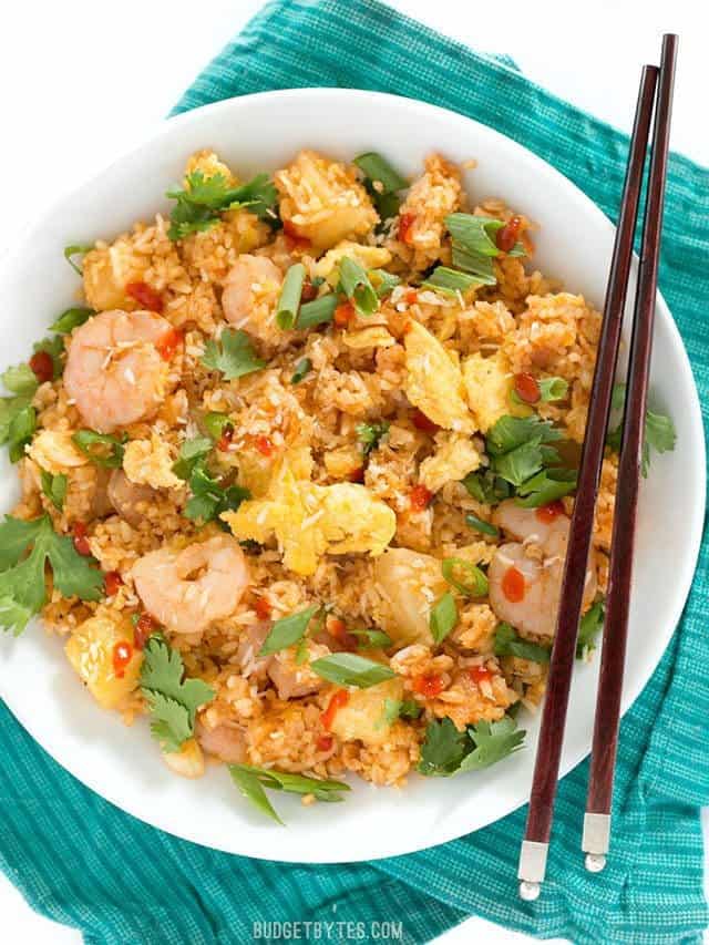 Shrimp Fried Rice with Pineapple and Toasted Coconut is a fast and easy alternative to takeout, perfect for busy weeknights! BudgetBytes.com Overhead view of a large bowl full of Shrimp Fried Rice with Pineapple and Toasted Coconut on a teal napkin with wooden chopsticks