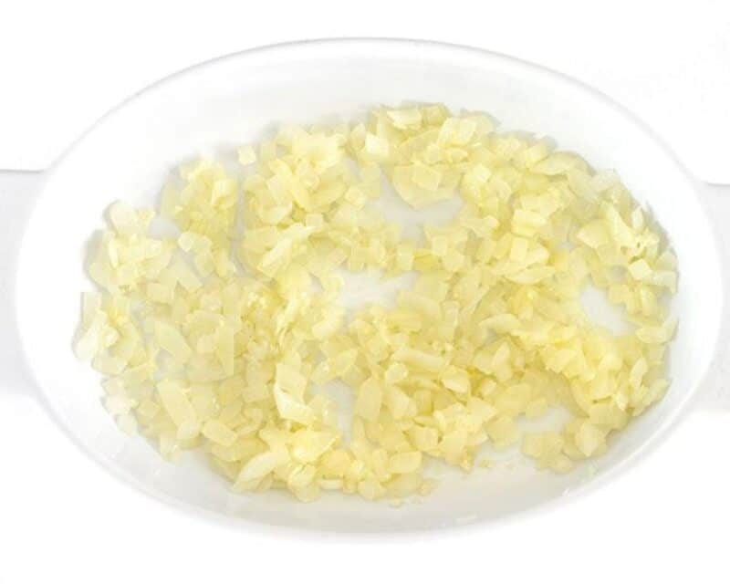 Sauteed onions and garlic in a white baking dish.