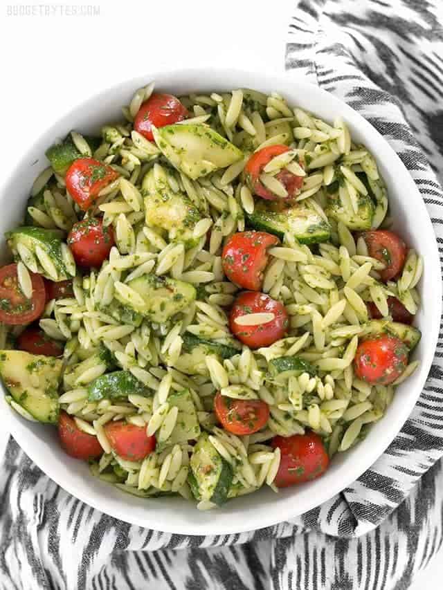 Zucchini and Orzo Salad with Chimichurri is a fresh summer salad that makes the perfect fresh and zesty side dish for summer grilling. BudgetBytes.com Overhead view of a bowl full of Zucchini and Orzo Salad with Chimichurri, on a black and white striped napkin