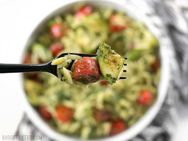 Zucchini and Orzo Salad with Chimichurri is a fresh summer salad that makes the perfect fresh and zesty side dish for summer grilling. BudgetBytes.com Close up of a forkful of Zucchini and Orzo Salad with Chimichurri with the bowl in the background
