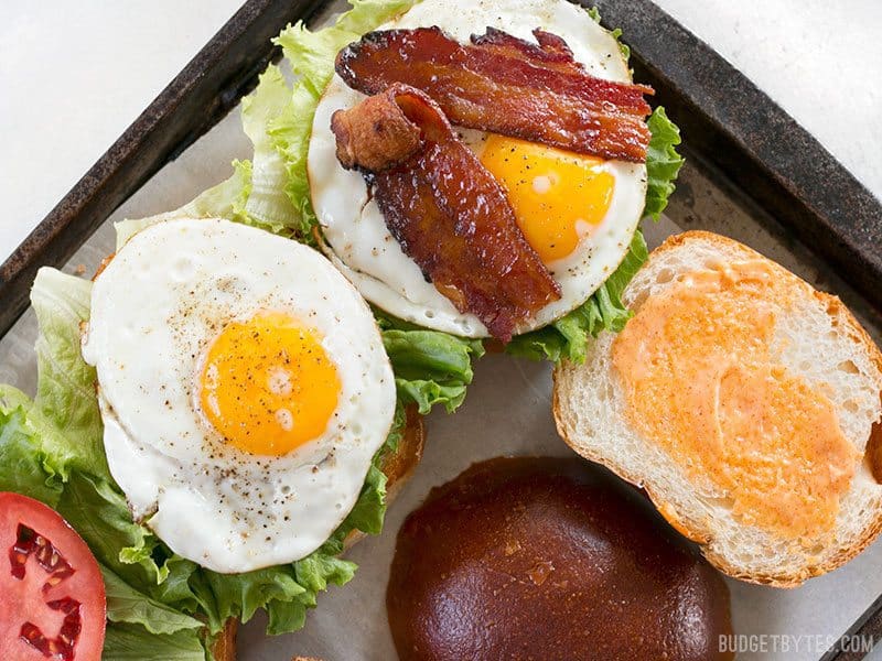Brown Sugar Bacon Breakfast Sandwiches with Chipotle Mayo are the perfect mix of salty, sweet, and spicy for your weekend brunch. BudgetBytes.com Brown Sugar Bacon Breakfast Sandwiches on a baking sheet being assembled