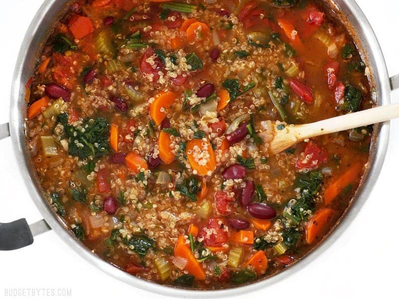 Garden Vegetable Quinoa Soup is a low calorie, high fiber, flavor packed meal perfect for your weekend meal prep. Freezer friendly and vegan! BudgetBytes.com Close up overhead view of the pot full of Garden Vegetable Quinoa Soup with a wooden spoon