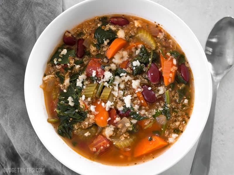 Garden Vegetable Quinoa Soup is a low calorie, high fiber, flavor packed meal perfect for your weekend meal prep. Freezer friendly and vegan! BudgetBytes.com A bowl full of Garden Vegetable Quinoa Soup topped with a little crumbled queso fresco