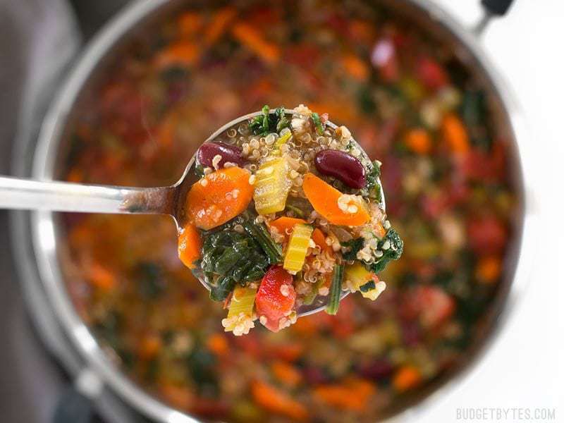 Garden Vegetable Quinoa Soup is a low calorie, high fiber, flavor packed meal perfect for your weekend meal prep. Freezer friendly and vegan! BudgetBytes.com Close up of a ladle full of Garden Vegetable Quinoa Soup with the pot in the background