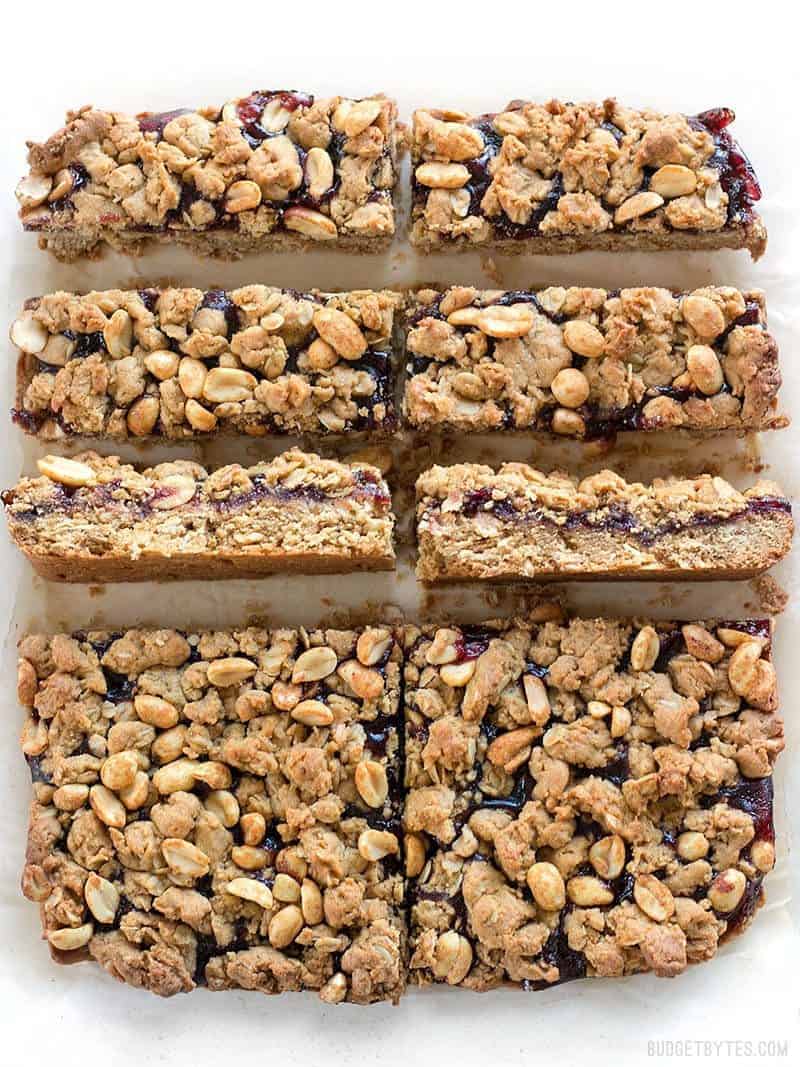 Peanut Butter and Jelly Bars are the perfect mix of salty and sweet in a dessert that will remind you of your childhood. BudgetBytes.com Peanut Butter and Jelly Bars cut from the slab, two turned sideways to make the layers visible.