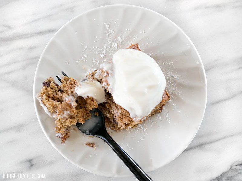 The 1917 Applesauce Cake from Anne Byrn's new book American Cake is light, sweet, and full of warm spices. BudgetBytes.com Overhead view of one slice of Applesauce Cake with a scoop of ice cream on top, being eaten with a fork.
