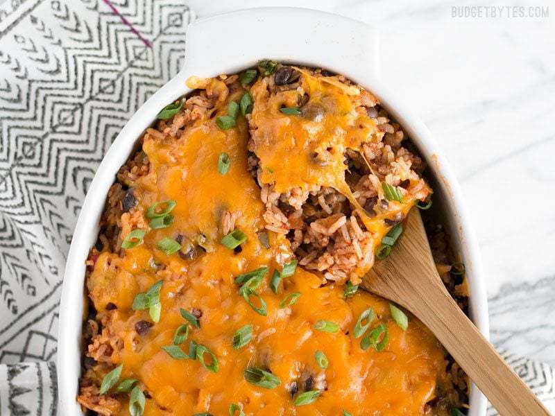 This Beef Burrito Casserole is totally customizable and can include all your favorite burrito or nacho toppings. Leftovers reheat great for lunch! Budgetbytes.com Overhead view of the Beef Burrito Casserole in a casserole dish, being scooped out with a wooden spoon.