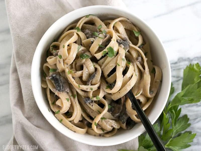 This rich and Creamy Mushroom Herb Pasta is a surprisingly fast and simple to way to have a gourmet meal at home. BudgetBytes.com Overhead of Creamy Mushroom Herb Pasta in a bowl with the pasta twirled around a black fork, parsley on the side