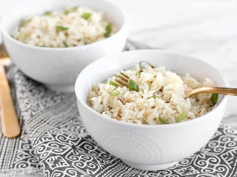 Cumin rice is an earthy and slightly peppery dish that can be used as the base for many meals. You'll never want to make plain rice again! BudgetBytes.com Two bowls of cumin rice, garnished with green onion, and two gold forks.