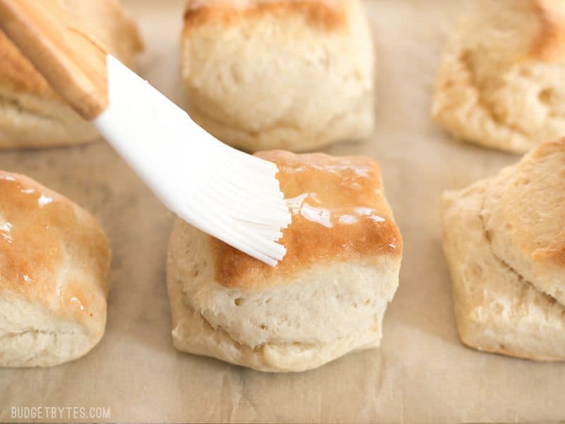 5 Ingredient Freezer Biscuits are the fastest and easiest way to have fresh, warm, and fluffy biscuits for breakfast any day of the week. BudgetBytes.com Melted butter being brushed onto a freshly baked Freezer Biscuit with a silicone brush