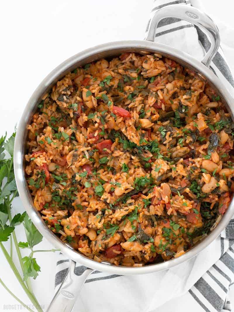 Tomato Herb Rice with White Beans and Spinach is a hearty and flavorful vegan dinner that will be loved by meat eaters and vegetarians alike. BudgetBytes.com A deep skillet full of Tomato Herb Rice with White Beans and Spinach, garnished with chopped parsley