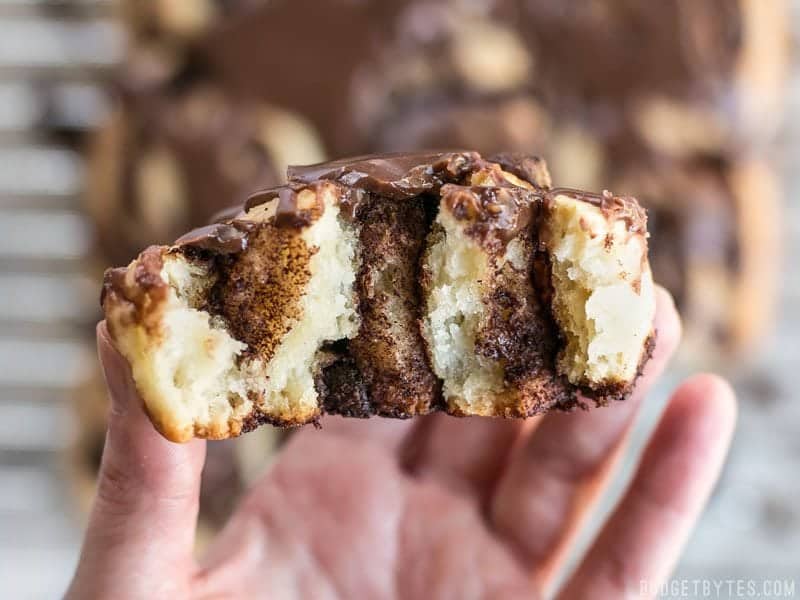 A 5 ingredient dough makes these chocolate cinnamon buns fast, easy, soft, and fluffy. The perfect treat for lazy weekend mornings! BudgetBytes.com Close up of a hand holding one chocolate cinnamon bun that has been torn in half so the inside is visible