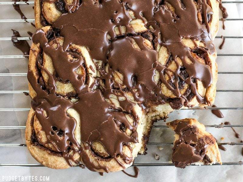 A 5 ingredient dough makes these chocolate cinnamon buns fast, easy, soft, and fluffy. The perfect treat for lazy weekend mornings! BudgetBytes.com chocolate cinnamon buns with chocolate icing, viewed from above, on a wire cooling rack