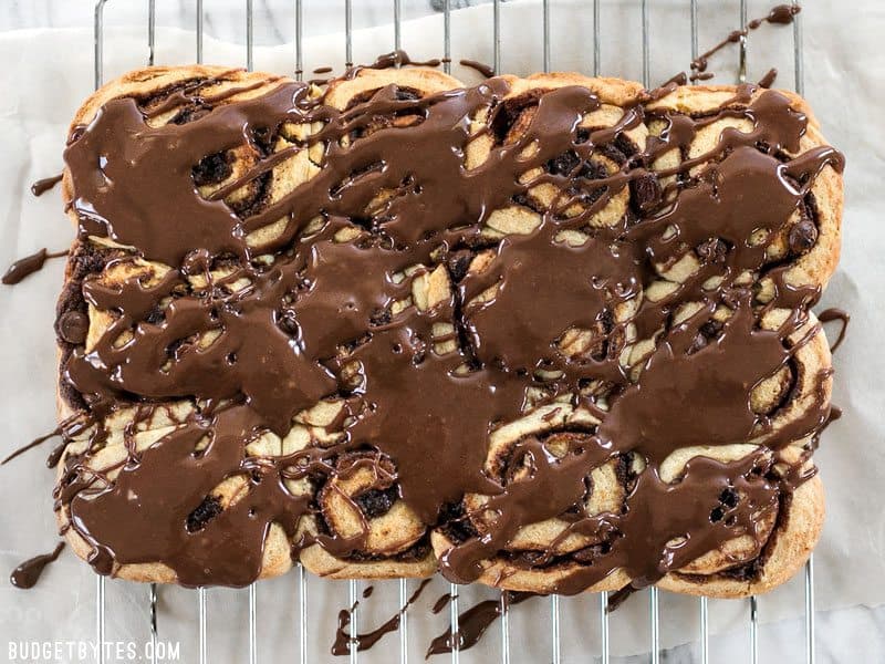 A 5 ingredient dough makes these chocolate cinnamon buns fast, easy, soft, and fluffy. The perfect treat for lazy weekend mornings! BudgetBytes.com 12 chocolate cinnamon buns drizzled with chocolate glaze, cooling on a wire rack