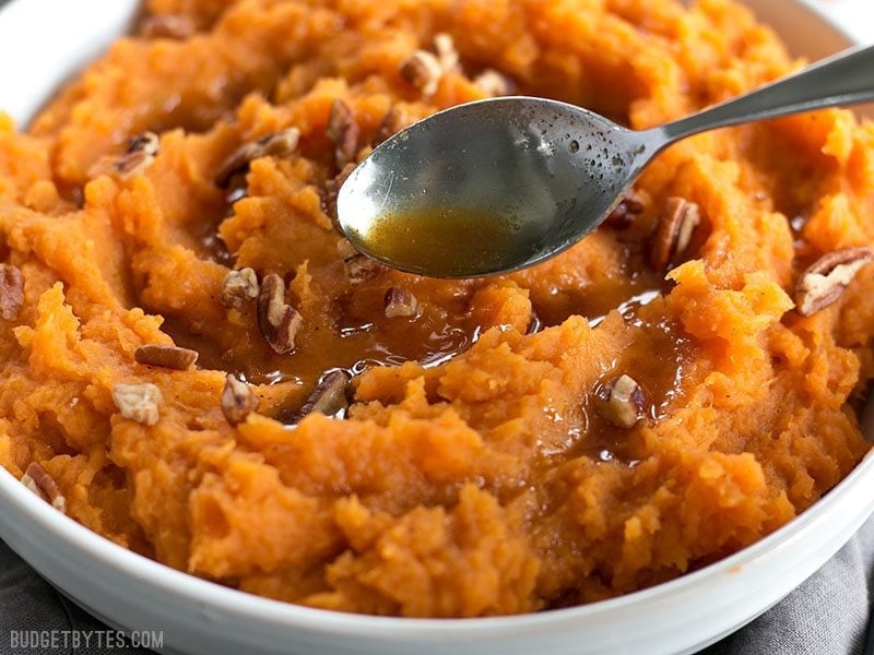 Maple Brown Butter Mashed Sweet Potatoes are a simple way to add a little something extra special to your Thanksgiving table. Easy, delicious, elegant. Budgetbytes.com Close up of Brown Butter being drizzled onto Mashed Sweet Potatoes.