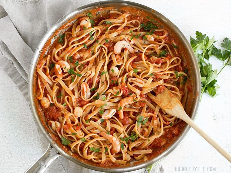 Spicy Seafood Pasta with Tomato Butter Sauce is a simple go-to weeknight dinner that can be made with pantry staples. BudgetBytes.com Spicy Seafood Pasta with Tomato Butter Sauce in the skillet with a wooden pasta fork and parsley on the side
