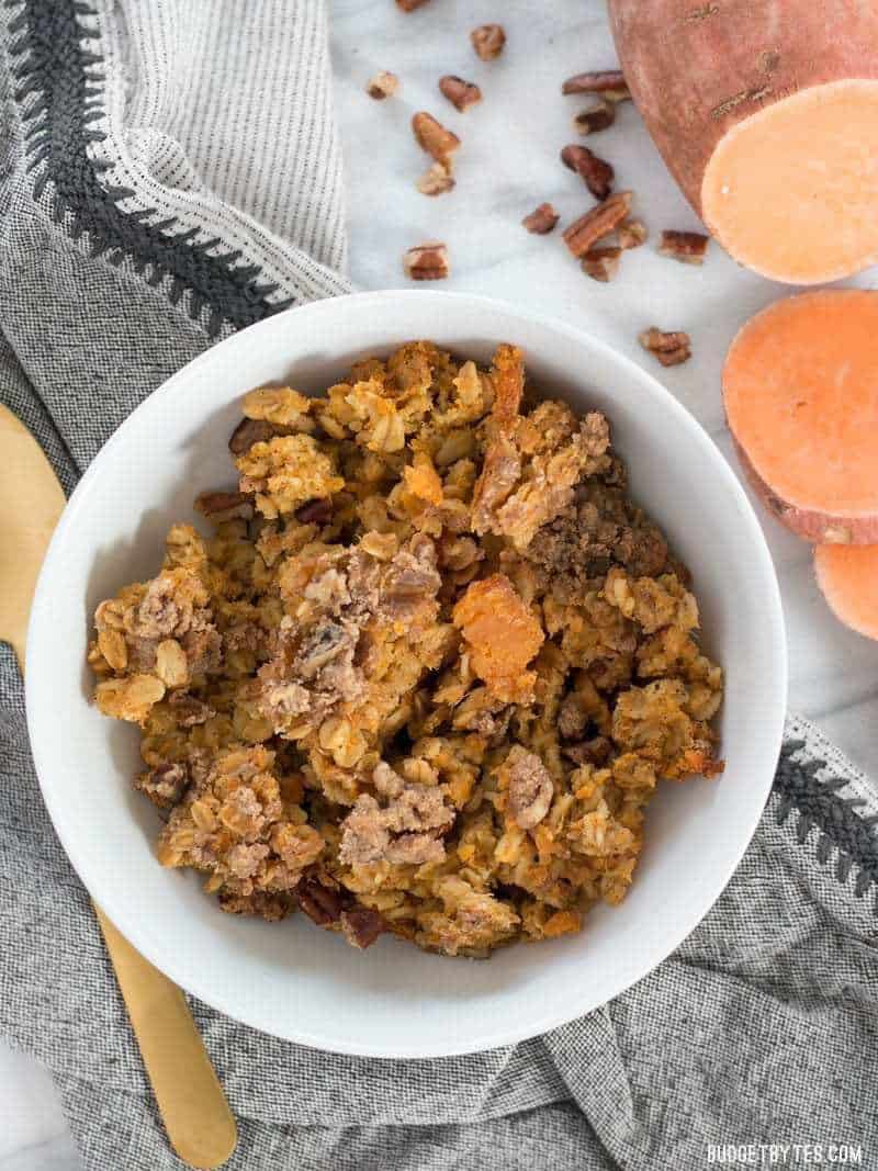 Sweet Potato Casserole Baked Oatmeal is a great way to have your favorite Thanksgiving side as a nutrient packed breakfast. BudgetBytes.com A bowl full of Sweet Potato Casserole Baked Oatmeal with a sliced fresh sweet potato on the side.