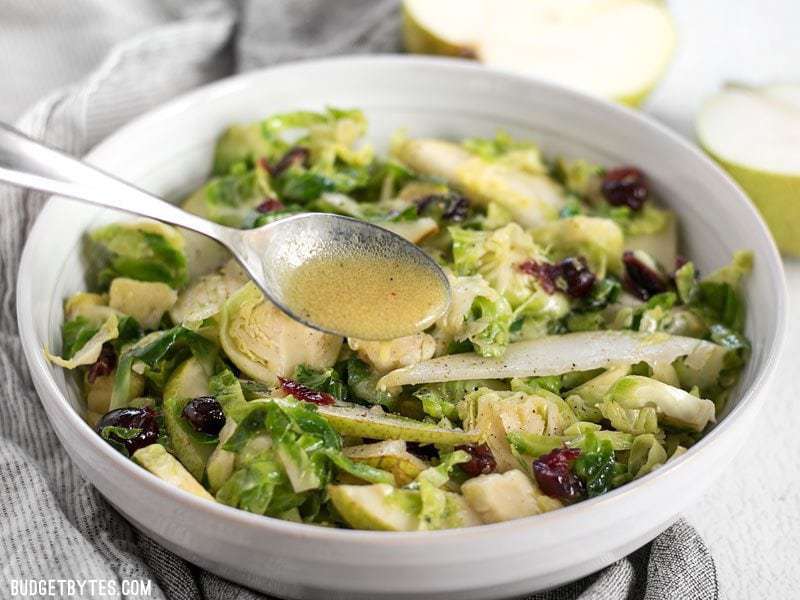 This Warm Brussels Sprouts and Pear Salad combines winter flavors in a warm and filling side dish. BudgetBytes.com Dijon vinaigrette being drizzled over a Warm Brussels Sprouts and Pear Salad