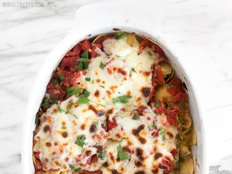 Baked Chicken with Artichokes and Tomatoes is an easy and flavorful weeknight dinner you can make with pantry staples. Budgetbytes.com Overhead shot of half of the Baked Chicken with Artichokes and Tomatoes in the casserole dish