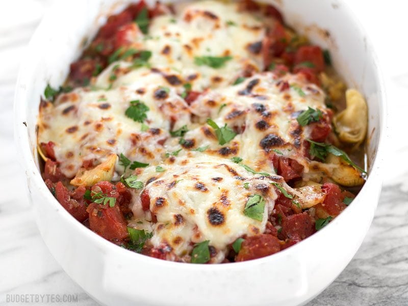 Baked Chicken with Artichokes and Tomatoes is an easy and flavorful weeknight dinner you can make with pantry staples. Budgetbytes.com Front view of the casserole dish full of Baked Chicken with Artichokes and Tomatoes