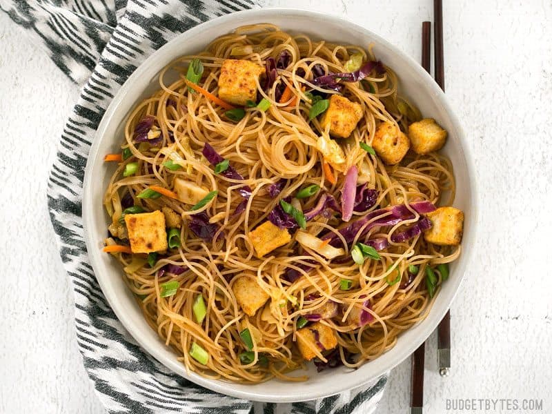 These Singapore Noodles with Crispy Tofu have a bold flavor and vibrant colors thanks to shredded vegetables and a bright curry sauce. BudgetBytes.com A bowl of Singapore Noodles with Crispy Tofu with chopsticks on the side