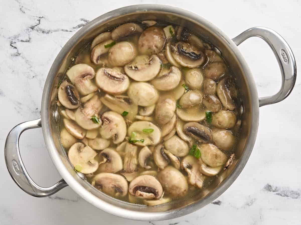 Broth added to sliced mushrooms and onions in a pot.