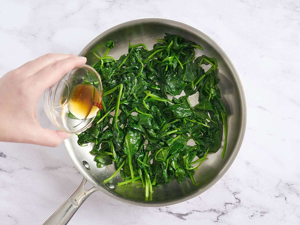 Sesame oil being drizzled on spinach in a skillet.