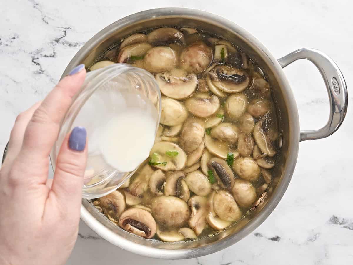 A cornstarch slurry being added to homemade egg drop soup in a pot.