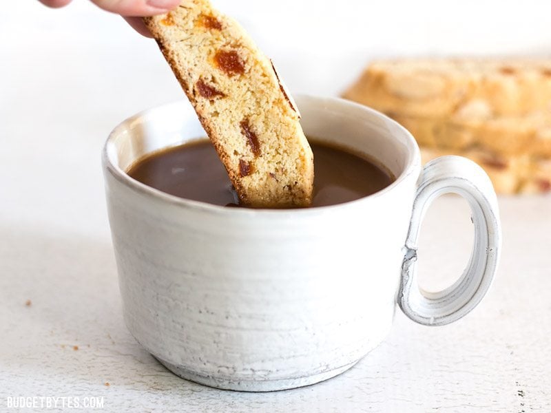 Fresh homemade Almond Apricot Biscotti are pennies a piece and can be stored in the freezer, ready for dunking at any time. BudgetBytes.com A piece of Almond Apricot Biscotti being dunked into a cup of coffee