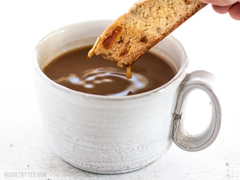 Fresh homemade Almond Apricot Biscotti are pennies a piece and can be stored in the freezer, ready for dunking at any time. BudgetBytes.com An Almond Apricot Biscotti dipped into a cup of coffee, dripping back into the cup