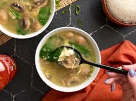 Overhead view of a bowl of egg drop soup with some on a black spoon.