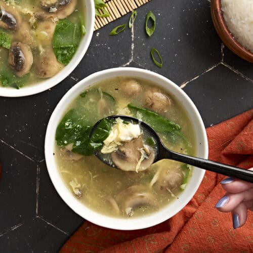 Overhead view of a bowl of egg drop soup with some on a black spoon.