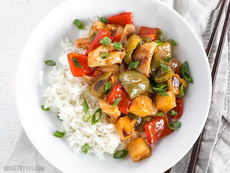 This oven baked Sheet Pan Sweet and Sour Chicken is a little more forgiving than a fast moving, high heat stir fry, making it great for beginners! BudgetBytes.com Sheet Pan Sweet and Sour Chicken in a bowl with rice, garnished with sliced green onions