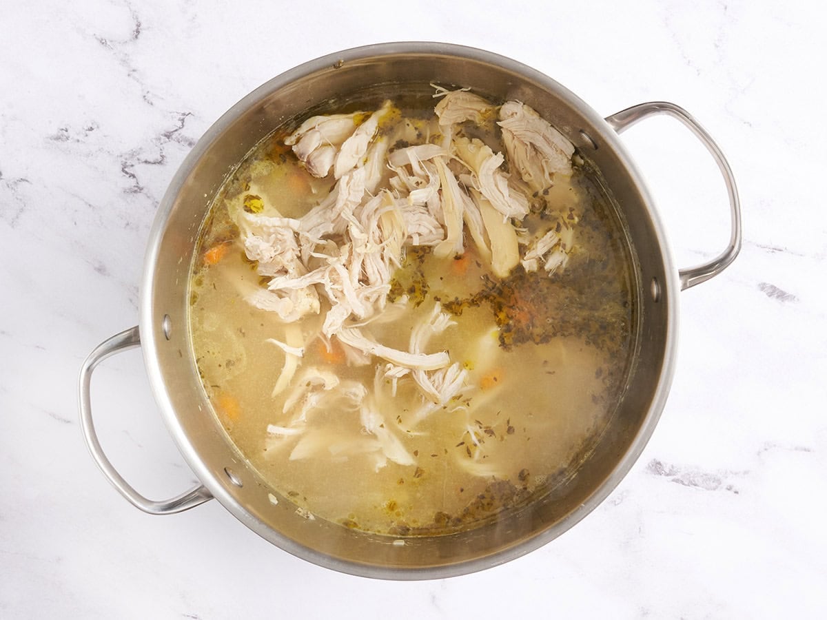 Shredded chicken added to a pot of chicken noodle soup.
