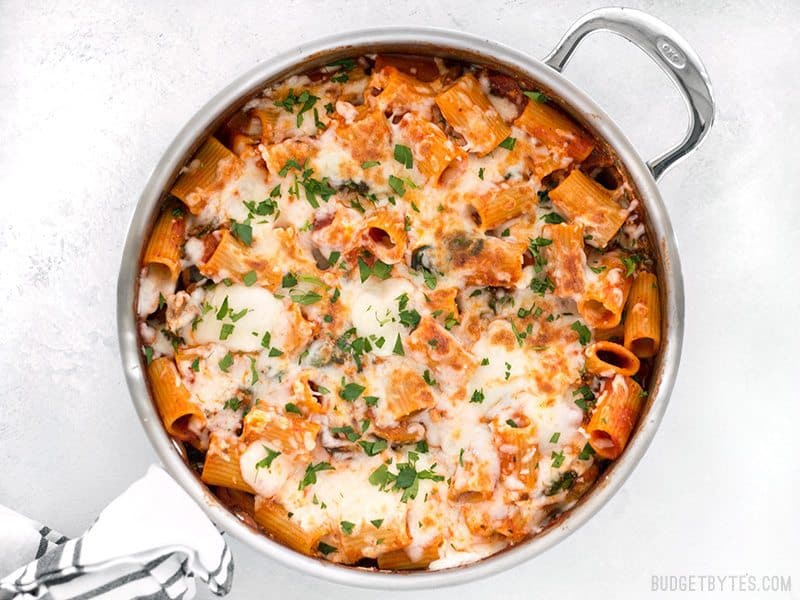 This Cheesy Rigatoni Skillet is a fast comfort meal for when you need dinner on the table fast! Like a fee-form lasagna packed with mushrooms and spinach. BudgetBytes.com Finished Cheesy Rigatoni Skillet garnished with parsley, a towel wrapped around the handle of the skillet