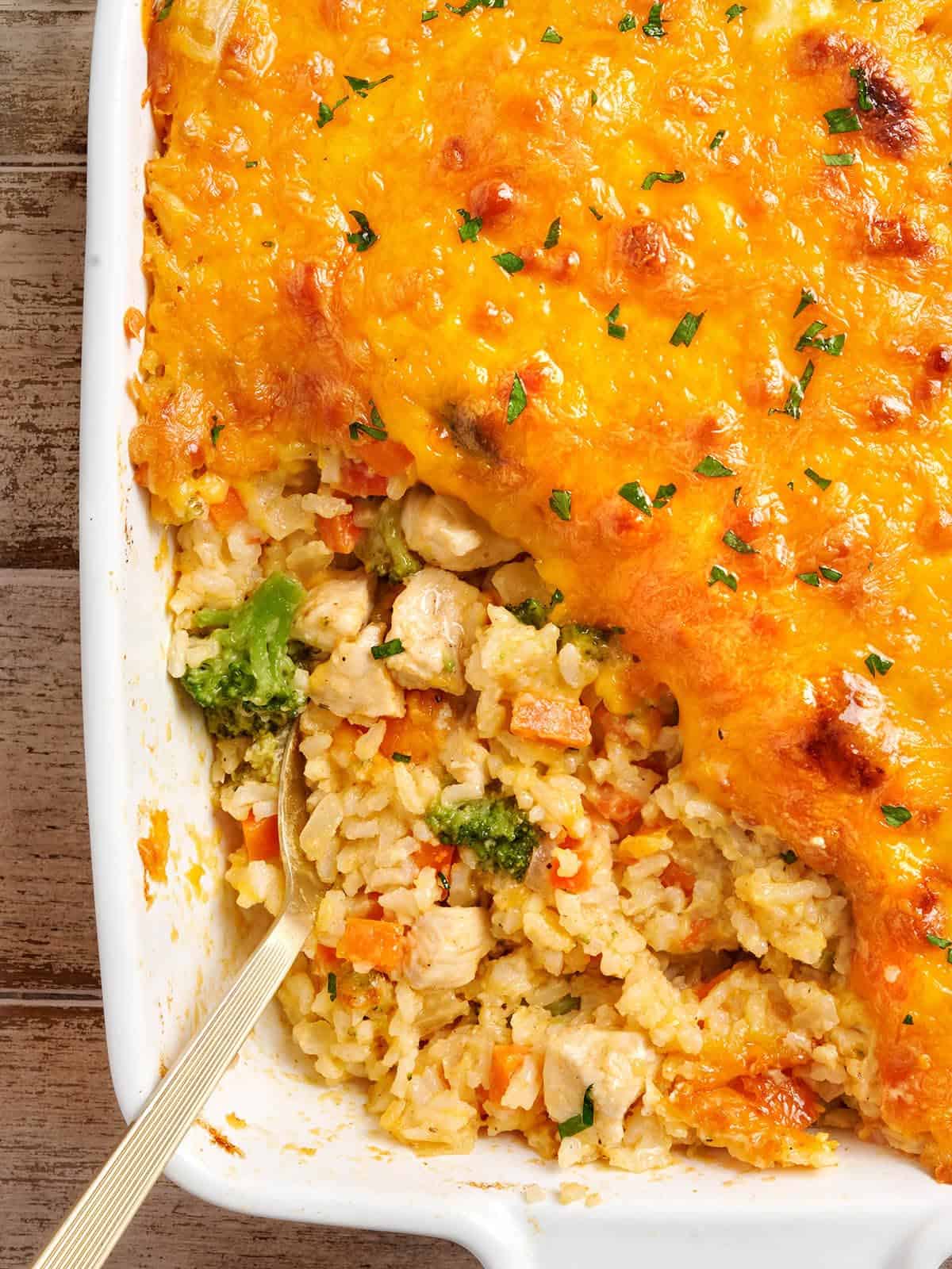 This Cheesy Chicken Vegetable and Rice Casserole is everything your comfort food dreams are made of. BudgetBytes.com Overhead view of chicken and rice casserole with a spoon.
