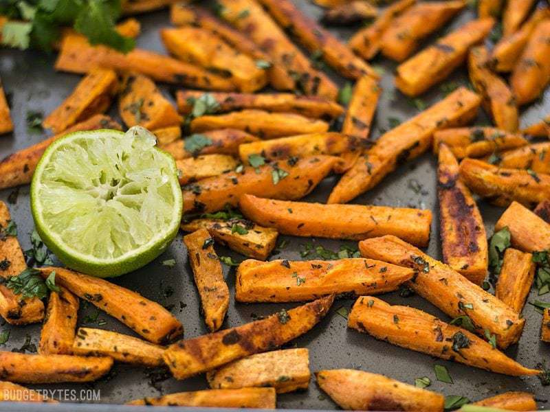 Bright lime juice and earthy cumin pair perfectly with the subtle creamy sweetness of sweet potatoes in these Cumin Lime Roasted Sweet Potatoes. BudgetBytes.com Close up side view of Cumin Lime Roasted Sweet Potatoes on the baking sheet
