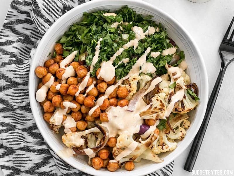 This Roasted Cauliflower Salad combines sweet roasted red onions, spiced chickpeas, tender cauliflower, and a tangy lemon tahini dressing. BudgetBytes.com Tahini dressing drizzled over a bowl of Roasted Cauliflower Salad