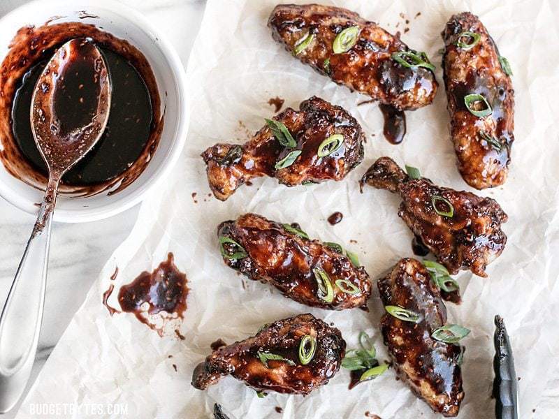 These crispy Raspberry Balsamic Baked Chicken Wings are baked, not fried, and slathered in a sweet, tangy, and rich homemade sauce. BudgetBytes.com Raspberry Balsamic Baked Chicken Wings on parchment next to a bowl of balsamic sauce with a spoon