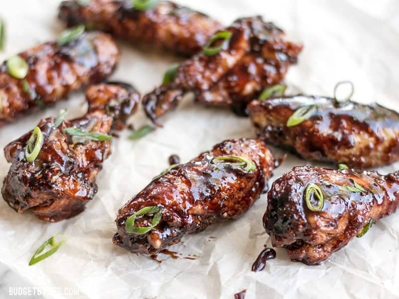 These crispy Raspberry Balsamic Baked Chicken Wings are baked, not fried, and slathered in a sweet, tangy, and rich homemade sauce. BudgetBytes.com Front view of Raspberry Balsamic Baked Chicken Wings on parchment with sliced green onions