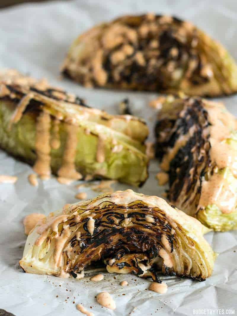 Blackened Cabbage is a fast and simple side dish that pairs beautifully with any grilled or BBQ meat. Add a creamy chipotle mayo for extra punch. BudgetBytes.com Wedges of Blackened Cabbage on parchment with chipotle sauce drizzled over top